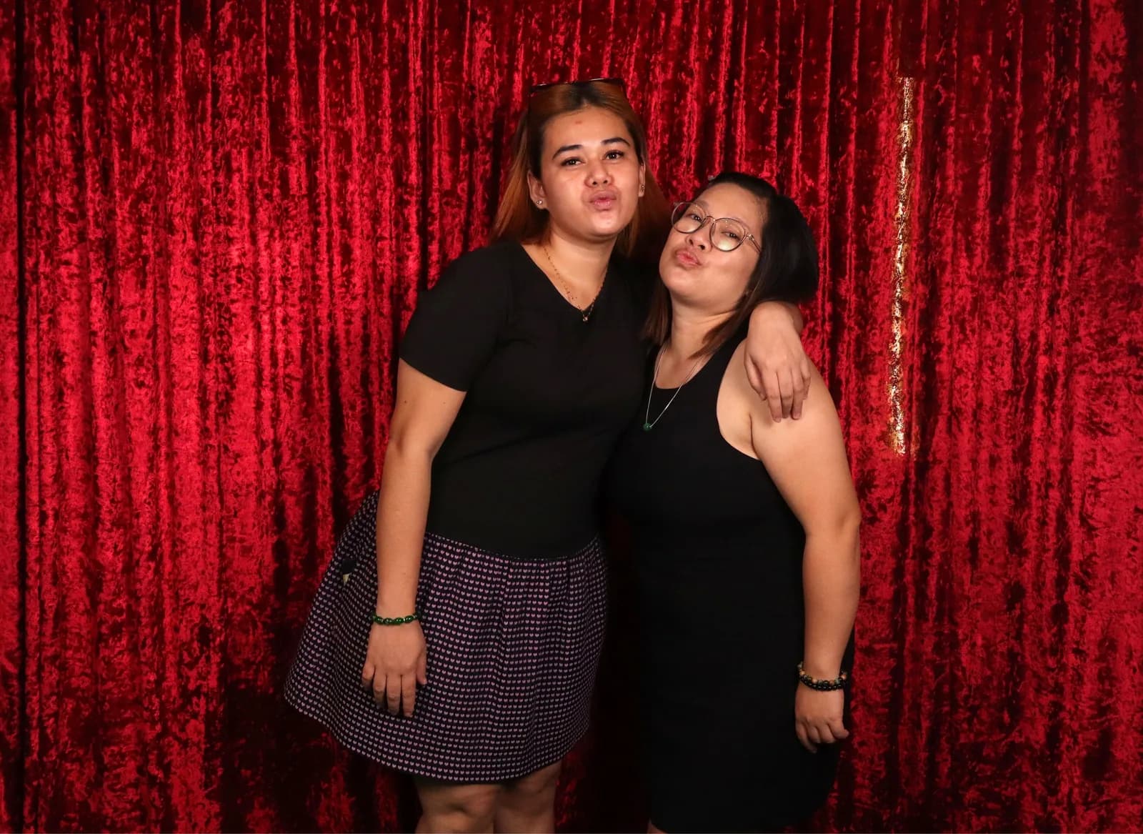Two friends sharing a playful pose in front of a red backdrop